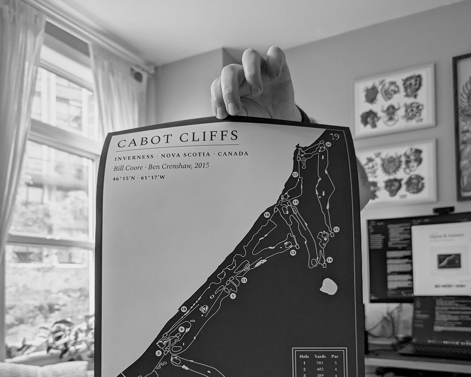 A hand-drawn Cabot Cliffs print held up in front of a wall of tattoo flash.